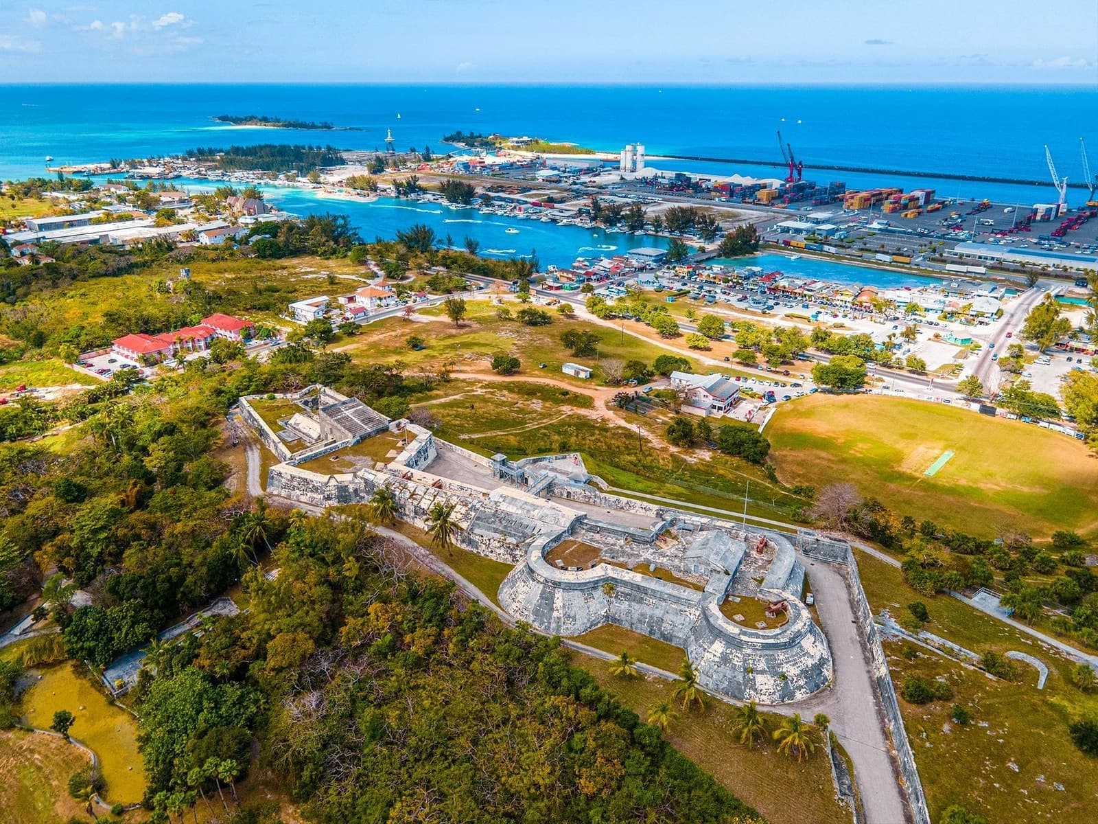 Aerial view of a coastal fortress and harbor with lush greenery and blue ocean